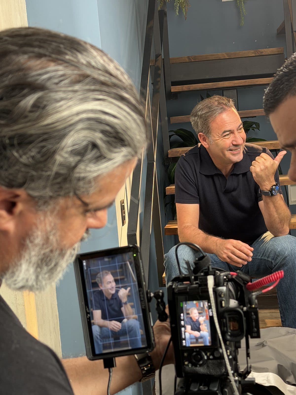 Adam Rozen smiling on a film set while a camera operator in the foreground frames him on a monitor.