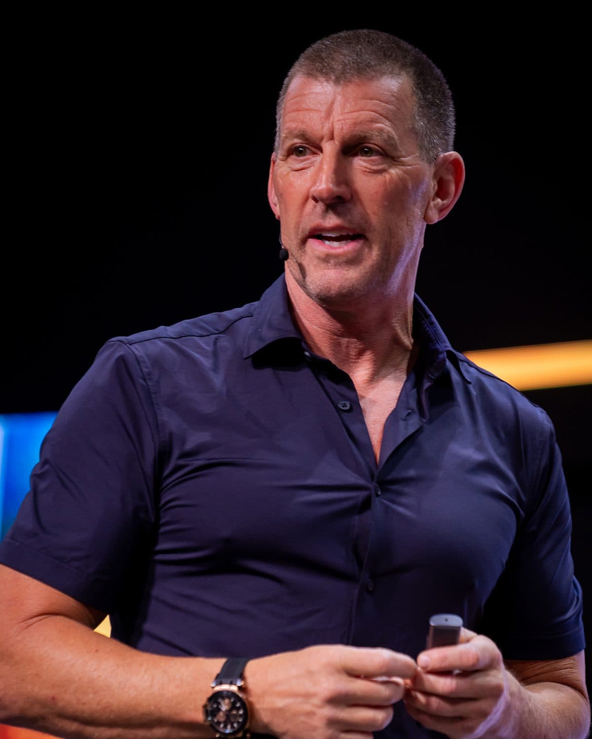 Dan Metcalfe speaking on stage with a headset microphone and a presentation clicker.
