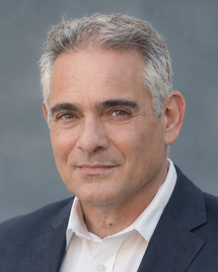 Ronen Hoffman in a navy jacket and open-collar shirt, photographed against a grey wall.